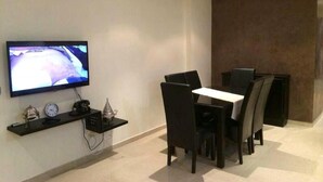 Een moderne eetruimte met een flatscreen televisie aan de muur, een klein plankje met een klok en decoratieve objecten, en een tafel met stoelen.