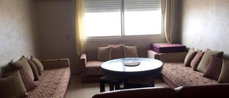 Sala de estar con un sofá, una mesa de centro redonda y una ventana con persianas.