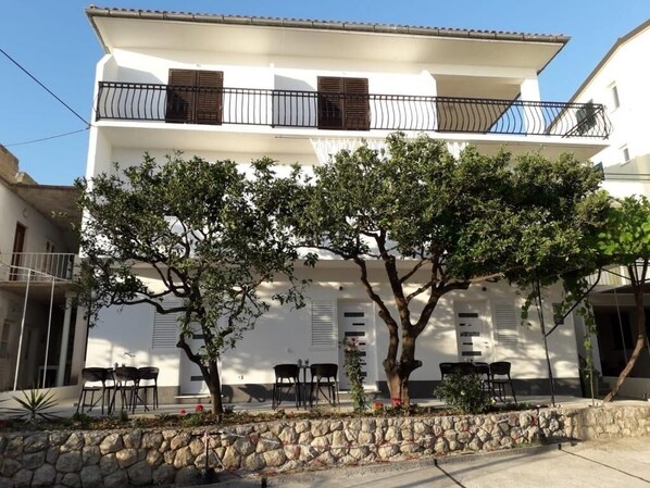 A two-story building with a white facade, a stone retaining wall, and outdoor seating area with tables and chairs.