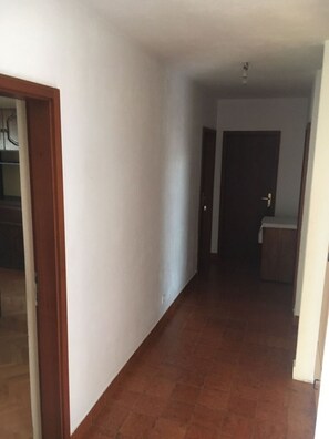 A hallway with a tiled floor, a wooden door, and a white wall.