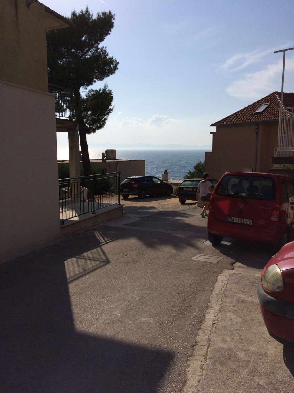 Eine Wohnstraße mit Blick auf das Meer, parkgeparkten Autos und einem Gebäude mit Balkon.