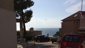 Une rue résidentielle donnant sur la mer, avec des voitures garées et un immeuble doté d’un balcon.