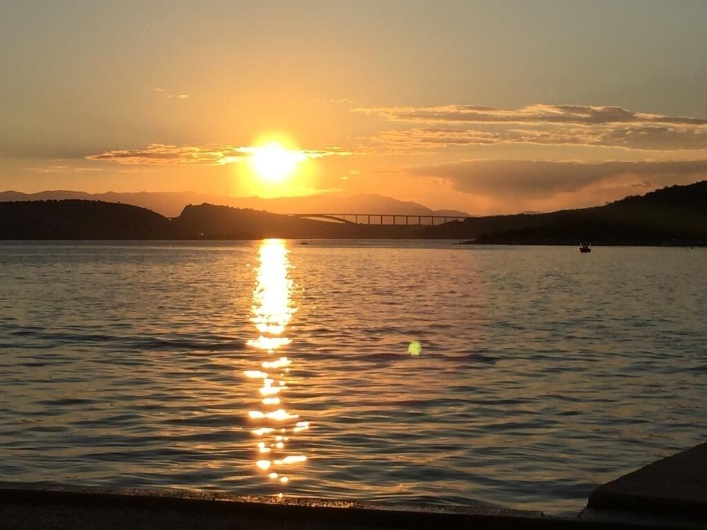 Ein Sonnenuntergang über ruhigem Wasser, im Hintergrund eine Brücke.