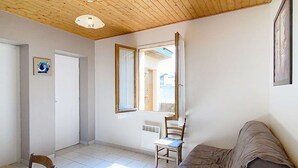 A room with a wooden ceiling, a dining table with chairs, a sofa, and a window with a view of the outside.