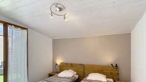 A room with two single beds, a wooden ceiling, a small table, and a nightstand.