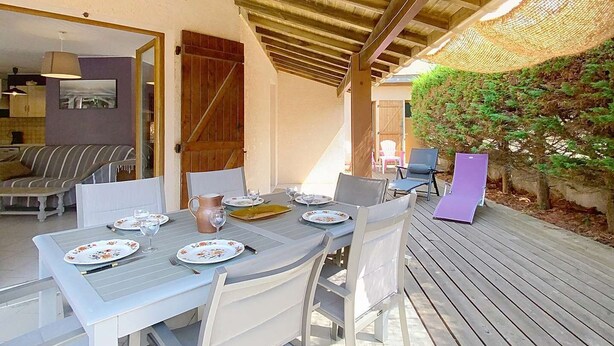 An outdoor dining area with a wooden ceiling, white table and chairs, and a view of the garden.