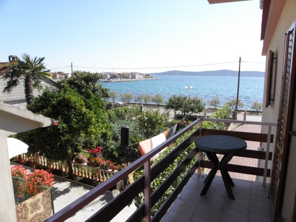 A balcony with a view of the sea, a table, and potted plants.