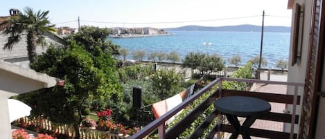 A balcony with a view of the sea, a table, and potted plants.