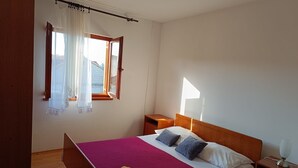 Un dormitorio con cama, mesita de noche, lámpara, ventana con cortinas y vistas al exterior.