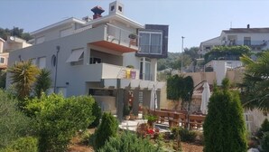 Un edificio moderno su due piani con balconi, un'area giardino con piante in vaso e cielo sereno.