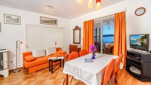 A living room with a sofa, dining table, and TV. There are curtains, a clock, and framed pictures on the walls. - Apartment in Pisak with Seaview, Terrace, Air condition, WIFI (102-4) (Pisak)