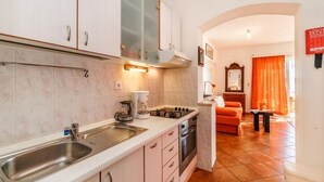 A compact kitchen with a sink, stove, and cabinets, leading to a living area with a sofa and orange curtains. - Apartment in Pisak with Seaview, Terrace, Air condition, WIFI (102-4) (Pisak)