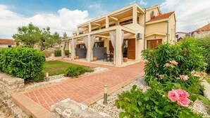 A two-story building with a covered patio area, a brick pathway, and surrounding greenery. - Apartment in Nin with Terrace, Air condition, WIFI (864-4) (Nin)