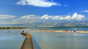 A beach with a wooden pier extending into calm waters, surrounded by mountains in the background. - Apartment in Nin with Terrace, Air condition, WIFI (864-4) (Nin)