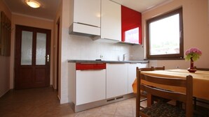 A kitchen with white cabinets, a red accent, a window, and a dining table with chairs. - Apartment in Poreč with Balcony, Air condition, WIFI (3794-5) (Porec)