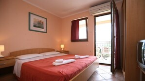 A hotel room with a double bed, a bedside table with a lamp, a window with a red curtain, and a balcony door. - Apartment in Poreč with Balcony, Air condition, WIFI (3794-5) (Porec)