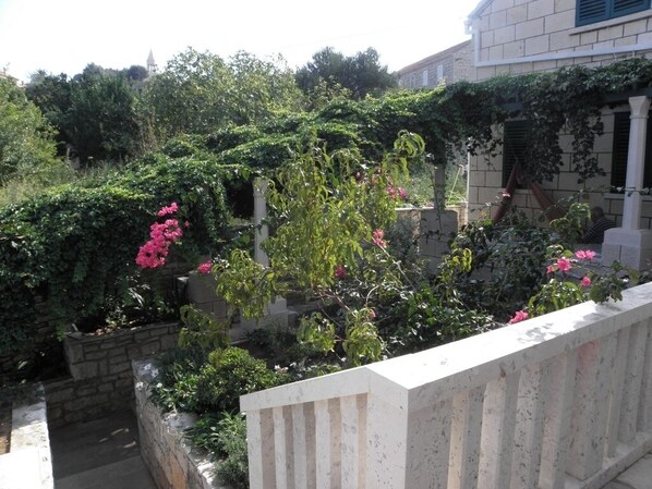 A garden with various plants and flowers, a stone wall, and a building in the background.