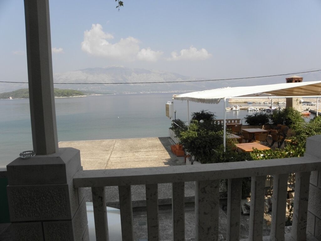 A terrace with a view of the sea, outdoor seating, and a building with a white roof.