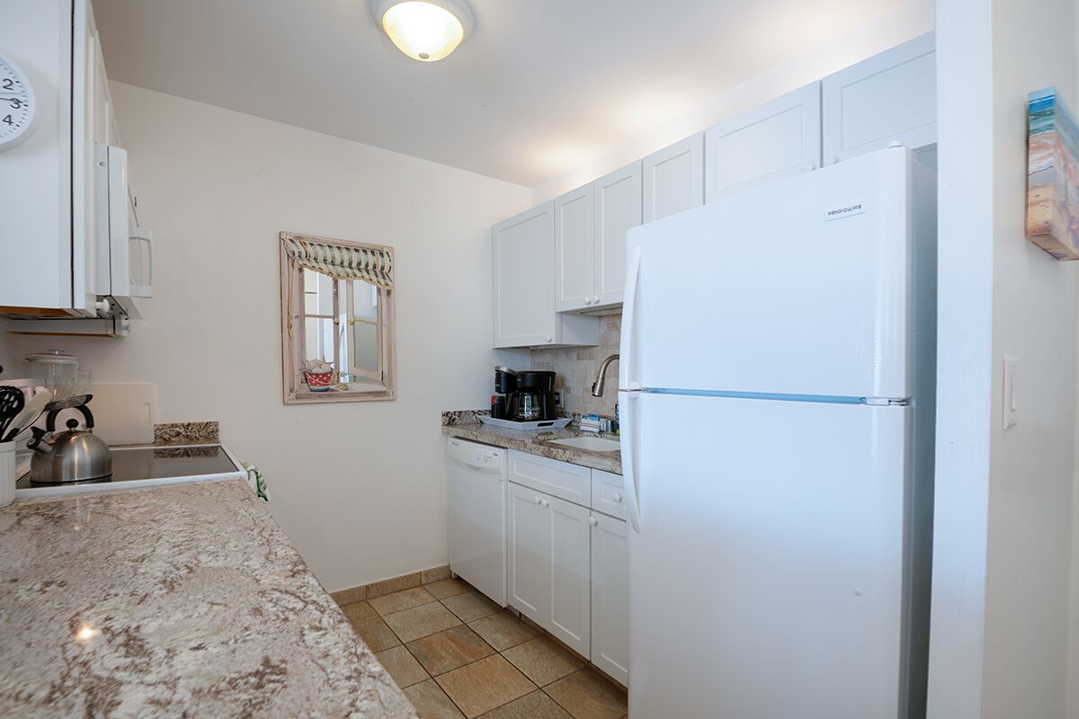 Una cocina con armarios blancos, un refrigerador blanco, una encimera de granito y un ventanal con marco decorativo.