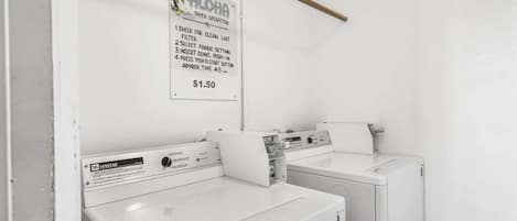 A laundry area with two white washing machines, a sign detailing the dryer's operation, and a price tag of $1.50.