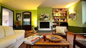 Un salon avec un canapé, une table basse sur laquelle sont posés des magazines et une assiette de nourriture, une cheminée et une bibliothèque remplie de livres.