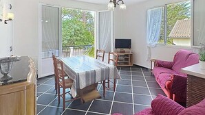 A room with a dining table, chairs, a sofa, a TV, and a balcony with curtains.