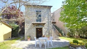 A stone building with a small patio, white chairs, and a staircase leading to an upper level. - Villa Sandia D: A welcoming apartment. (Castiglion fiorentino)