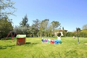 Un espace extérieur verdoyant avec une petite construction en bois, peut-être un abri de jardin, et un ensemble de jouets représentant un train coloré.