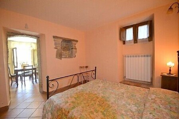 A bedroom with a bed, a radiator, a window, and a table with chairs.