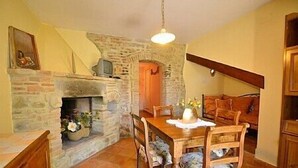 A cozy dining area with a stone fireplace, wooden dining table, and chairs. - Villa Sandia D: A welcoming apartment. (Castiglion fiorentino)