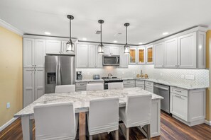 A modern kitchen with white cabinets, a stainless steel refrigerator, a microwave, and a dining area with a marble countertop and white chairs. - Partial Beach View 2 bed, 2 bath at Sanibel Moorings #1142 (Sanibel)
