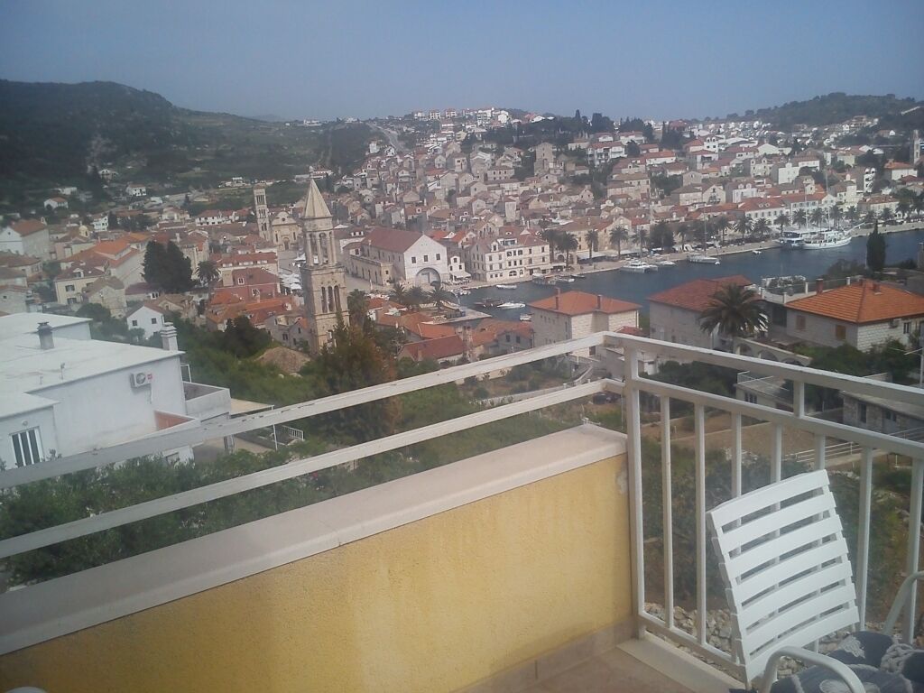 Un balcón con vistas a un pueblo costero, que incluye una iglesia destacada y un puerto deportivo.