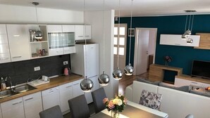 Een moderne keuken met witte kasten, een eetgedeelte met een strepen tafelkleed en een wand in turquoise.