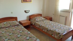 A bedroom with two single beds, a nightstand, a bedside table, a wall-mounted lamp, and a window with curtains.