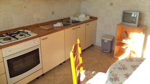 A kitchen with a stove, oven, sink, and a television on a stand.
