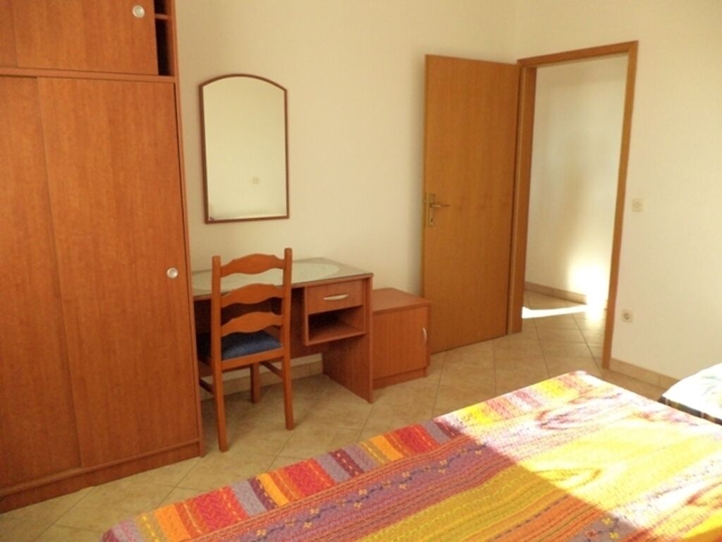 A bedroom with a bed, a wooden desk, a chair, a wardrobe, and a mirror.