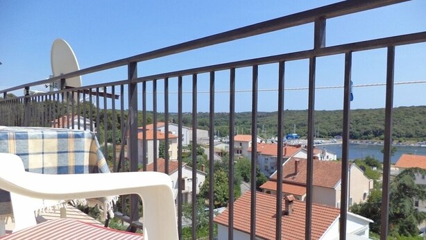 A balcony with a view of a coastal town, a white chair, and a table.