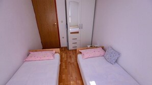 A small, narrow room with two single beds, a wooden floor, a white wardrobe, and a door. - Apartment in Podaca with Seaview, Terrace, WIFI (3676-1) (Podaca)