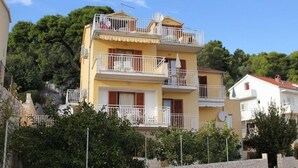 A multi-story building with balconies, a stone wall in the foreground, and trees in the background. - Apartment in Hvar town with Seaview, Terrace, Air condition, WIFI (3615-2) (Hvar)