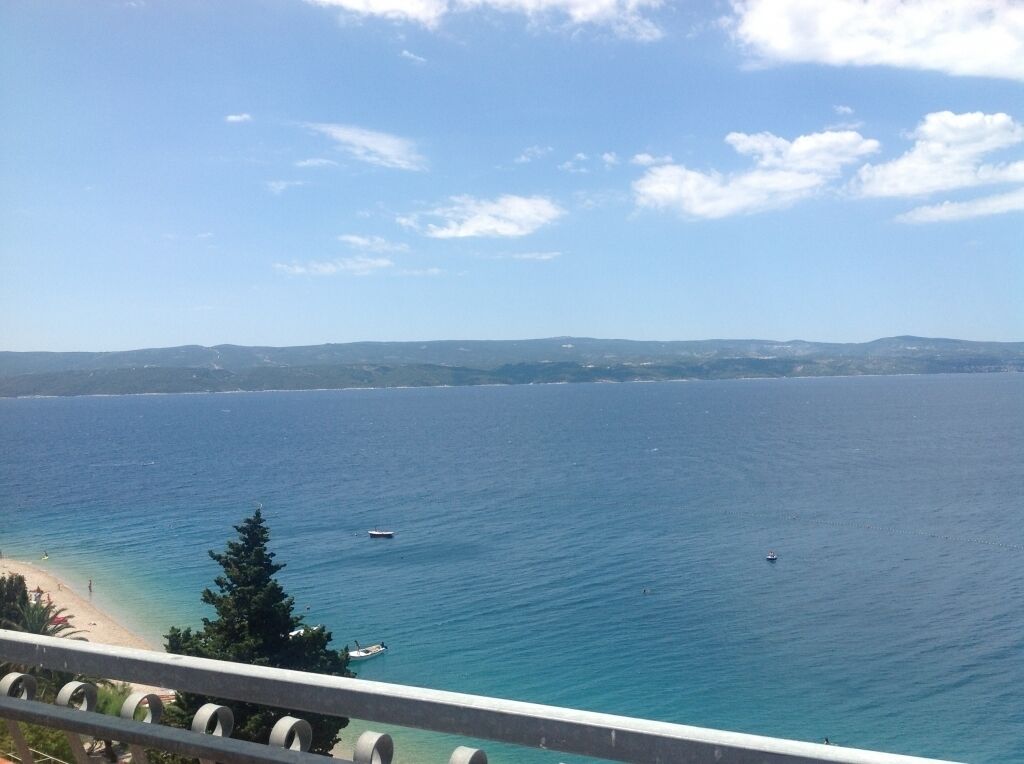 Küstensicht mit blauem Himmel, ruhiger See und weiter Küste im Hintergrund.