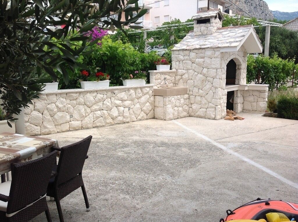 Un espacio al aire libre de piedra con una mesa y sillas, rodeado de plantas en macetas y un muro de piedra.