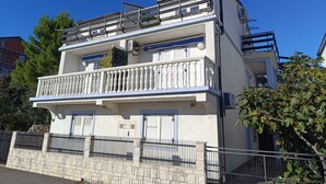 Un immeuble résidentiel à plusieurs étages, doté de balcons, d’une façade en pierre et surplombant un ciel d’un bleu éclatant.