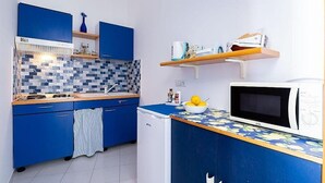 Eine kompakte Küche mit blauen Schränken, einer gefliesten Spritzschutzwand, einer Mikrowelle und einem kleinen Kühlschrank.