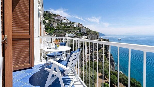Ein Balkon mit Tisch und Stühlen, mit Blick auf eine Küstenstadt und das Meer.