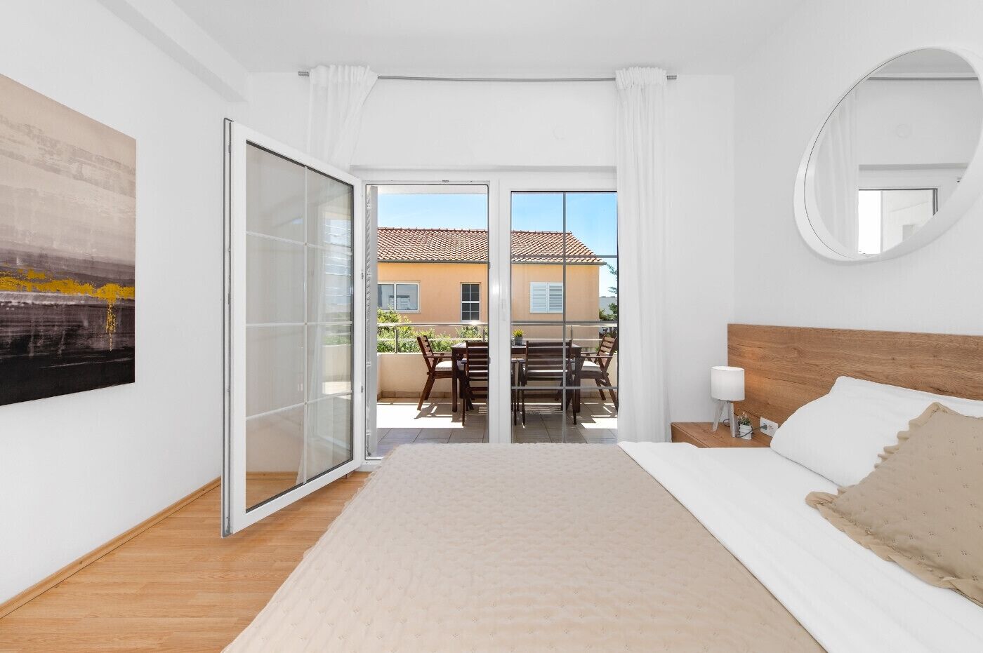 A bedroom with a bed, a bedside table, a mirror, a sliding glass door leading to an outdoor area with a table and chairs.