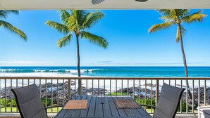 Ein Balkon mit Holztisch und -stühlen, der Blick auf einen Strand mit Palmen und Wellen geht.