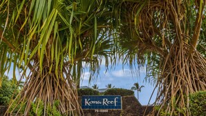Schild für Kona Reef, mit Steinmauer und tropischer Vegetation.