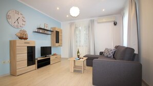 A modern living room with a grey sofa, wooden entertainment unit, and a wall clock. - Holiday Home in Poreč with Terrace, Air condition, WIFI, Dishwasher (4400-4) (Porec)
