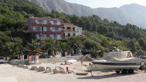 Ein Strand mit einem Boot, einem Gebäude und Bergen im Hintergrund.