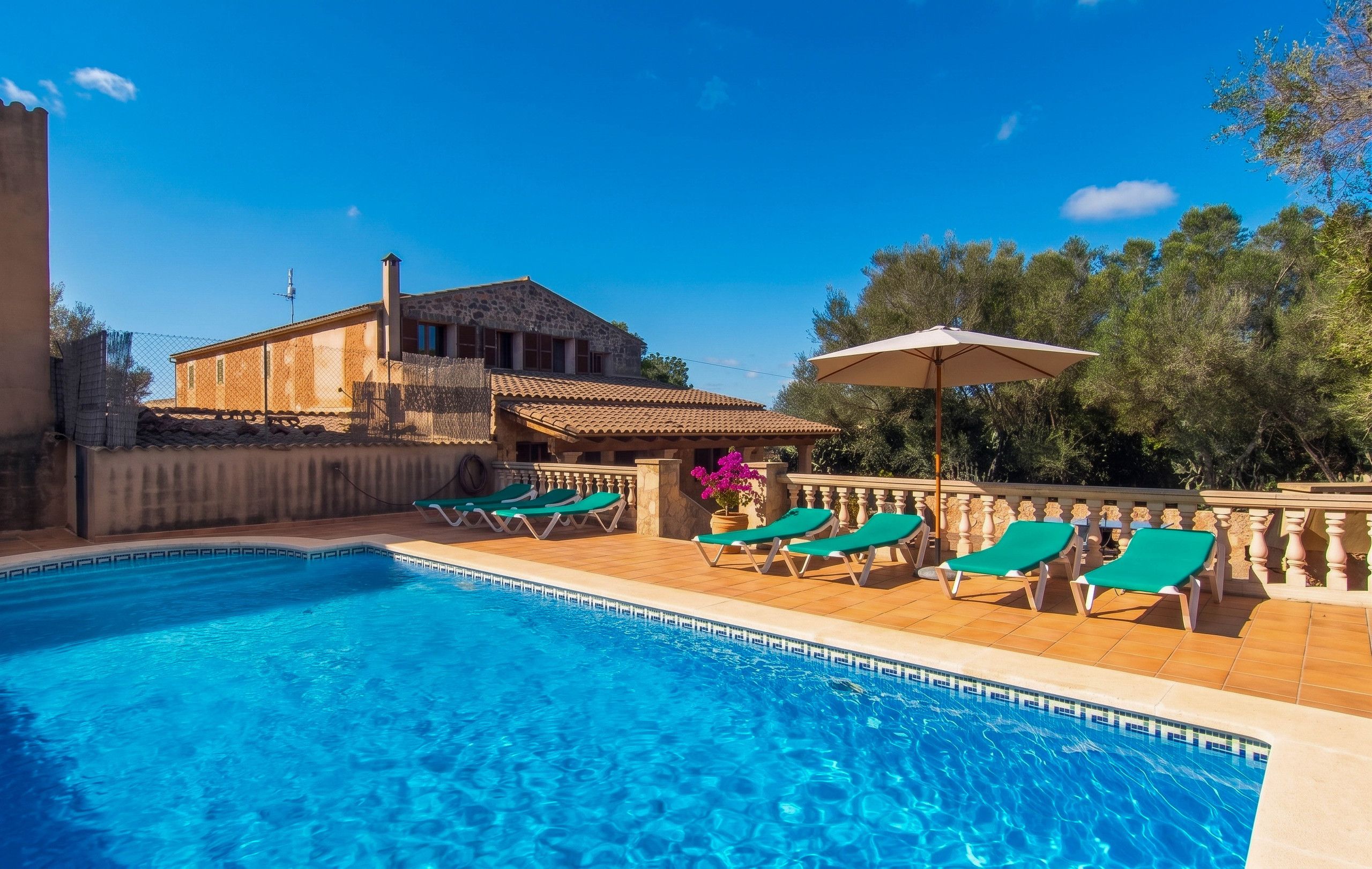 A swimming pool with clear blue water, surrounded by lounge chairs and a stone building.